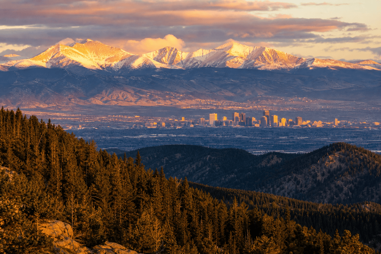 Colorado Rocky Mountain peaks at sunrise with Denver skyline visible in the valley