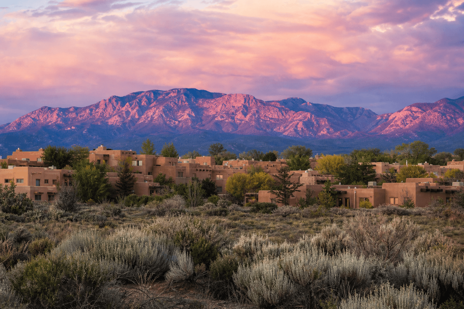New Mexico high desert at sunset with adobe buildings and Sandia Mountains glowing pink