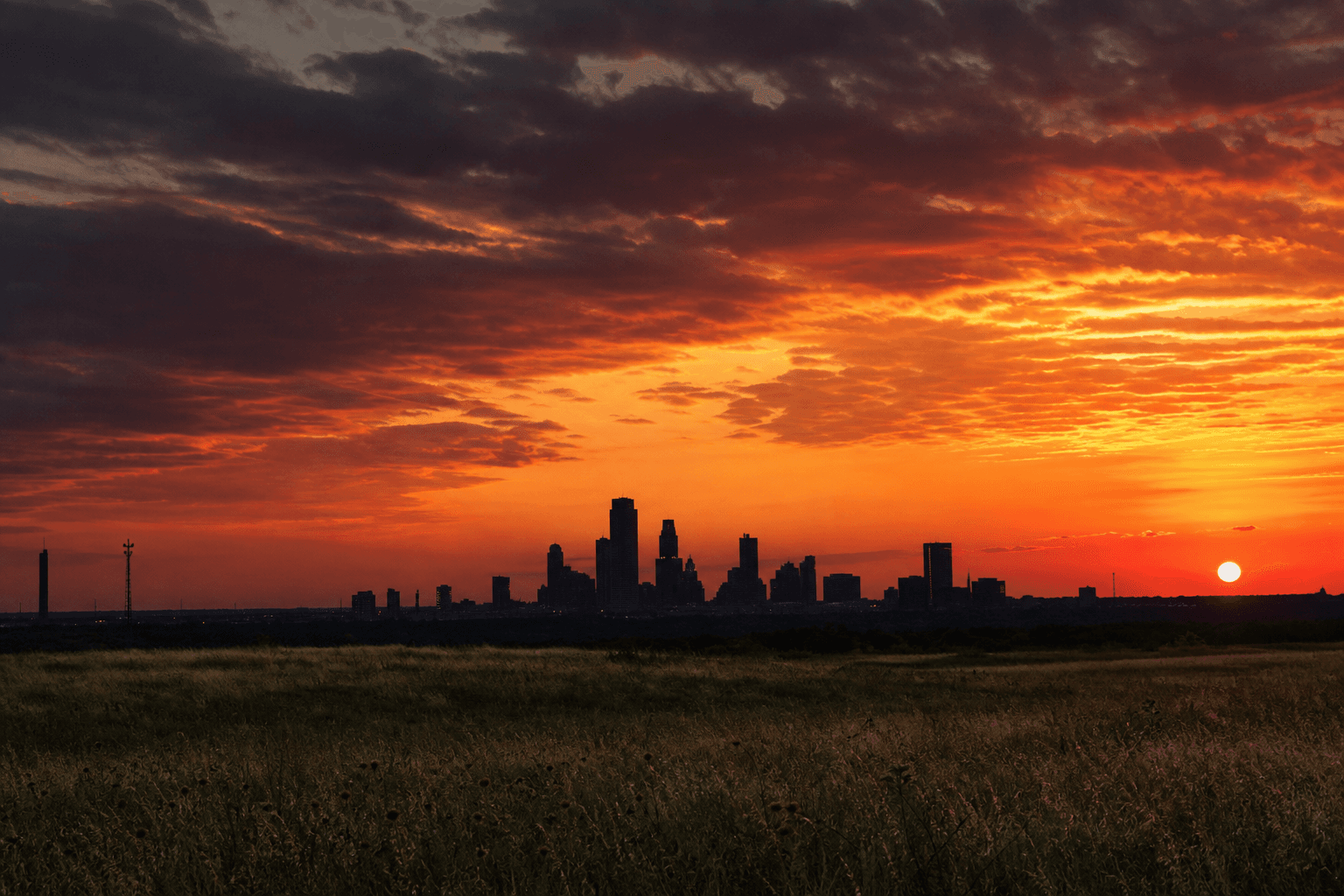 Oklahoma prairie sunset with a city skyline silhouette and dramatic crimson sky