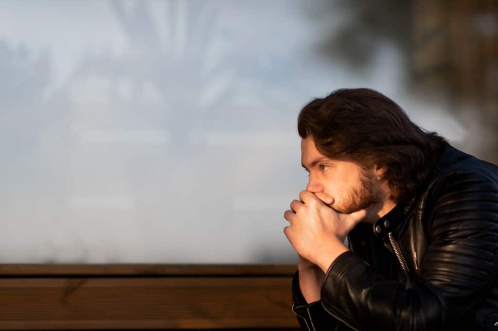 Pensive young man sitting and thinking outdoors