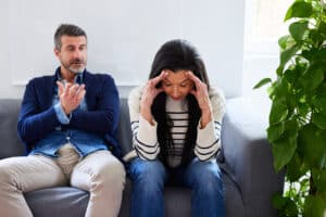 Frustrated wife with head in hands ignoring husband blaming her while sitting on sofa