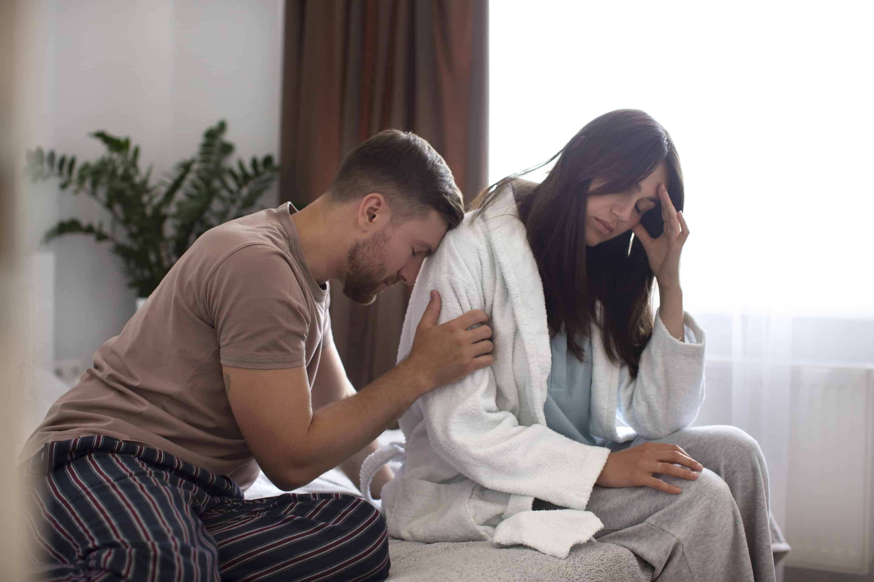 A woman struggling with addiction appears emotional while her partner looks on with concern, contemplating an intervention.